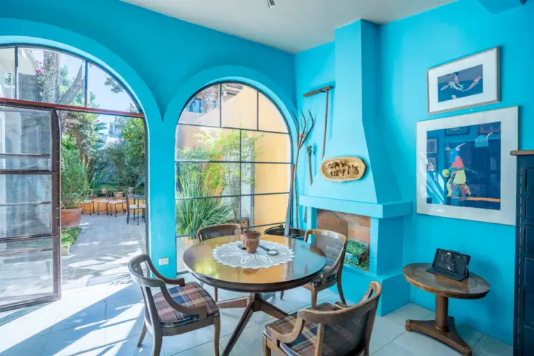 Casa Nispero, turquoise breakfast room with a fireplace, a round table and arched glass doors to the garden, San Miguel de Allende