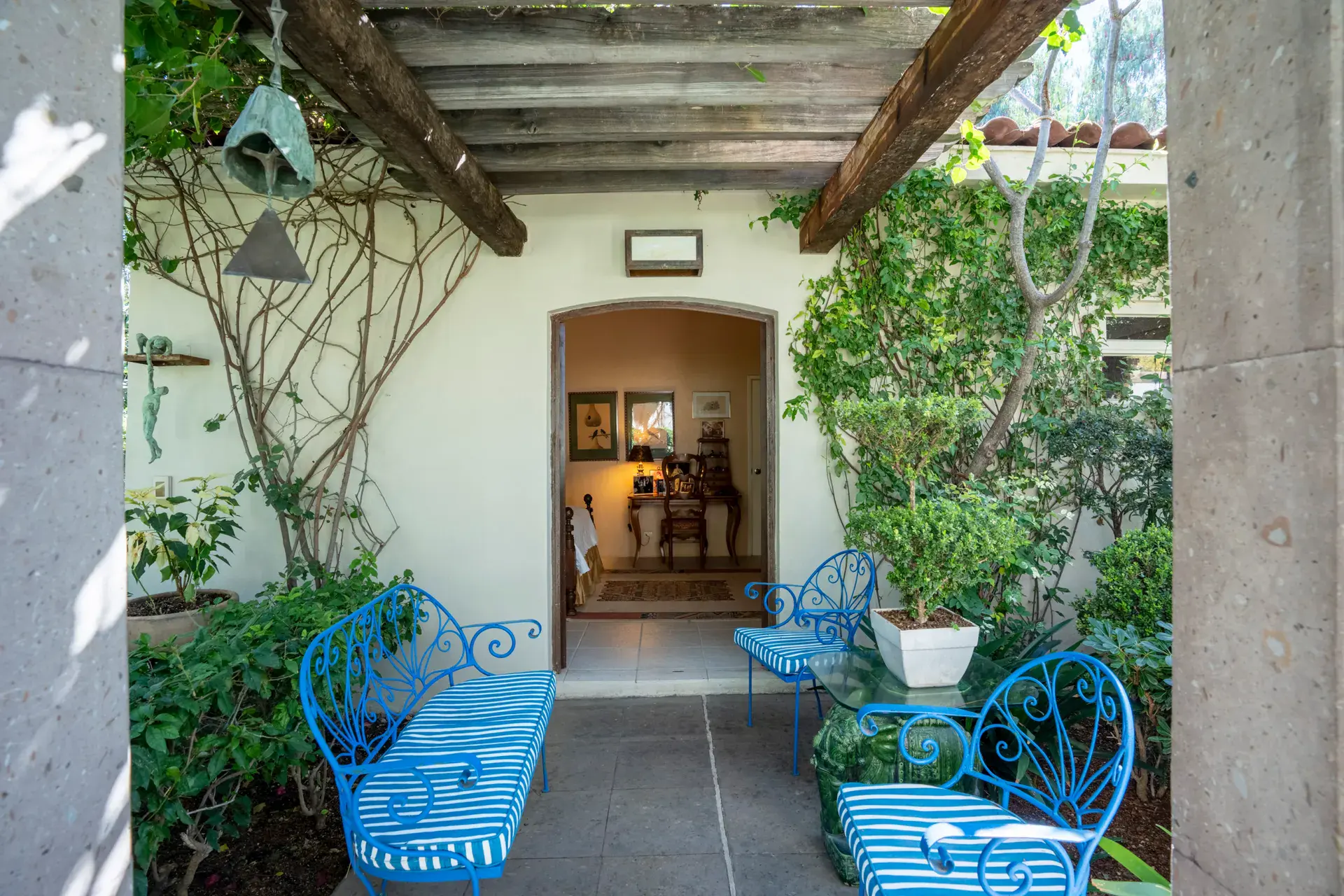 Casa Nispero, covered walkway with blue iron benches, a bell and climbing vines leading to an arched doorway, San Miguel de Allende