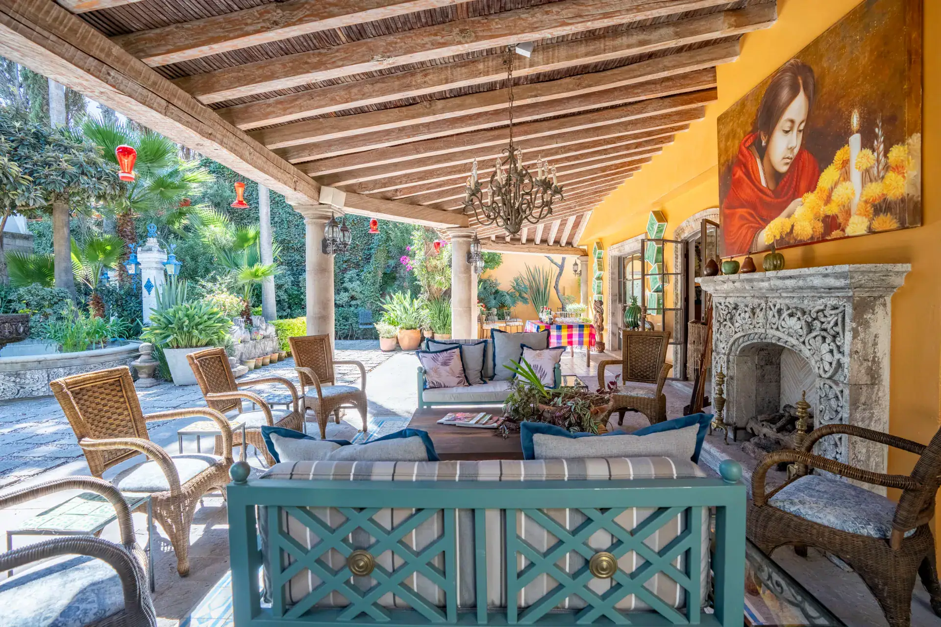 Casa Nispero, veranda with wicker chairs, a turquoise sofa, a carved stone fireplace and a portrait painting, San Miguel de Allende