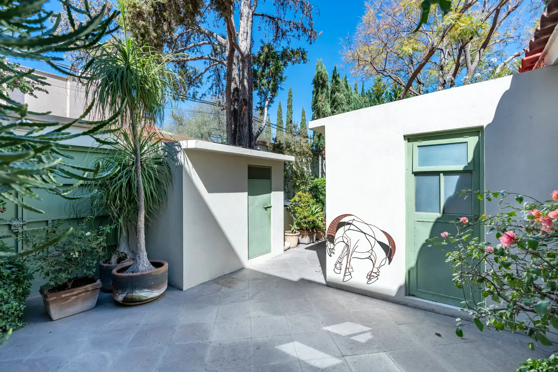 Casa Nispero, garden path beside a small white outbuilding with a green door and a horse drawing, San Miguel de Allende