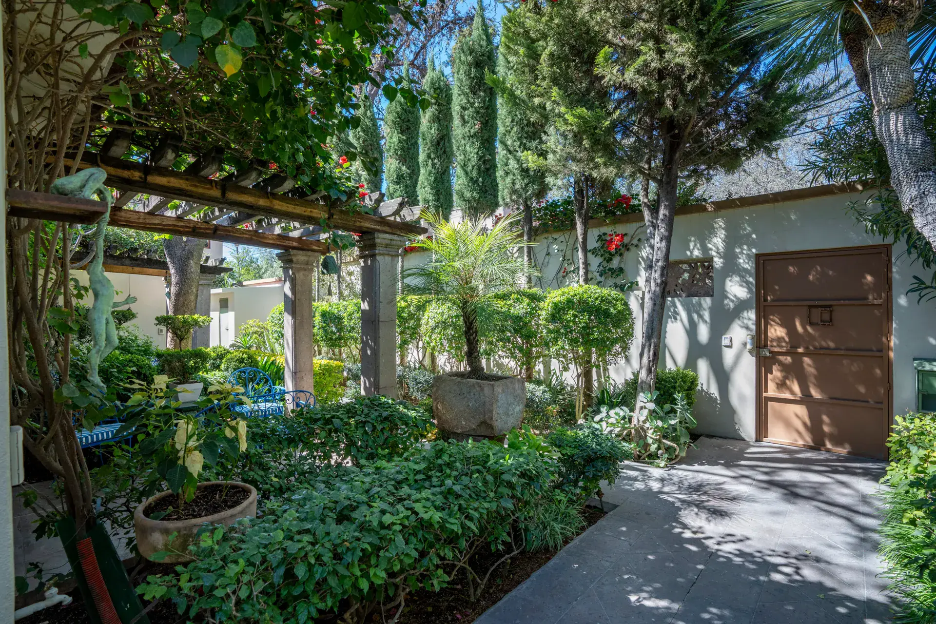 Casa Nispero, pergola walkway beside a stone planter, palms and a wood door in the garden, San Miguel de Allende
