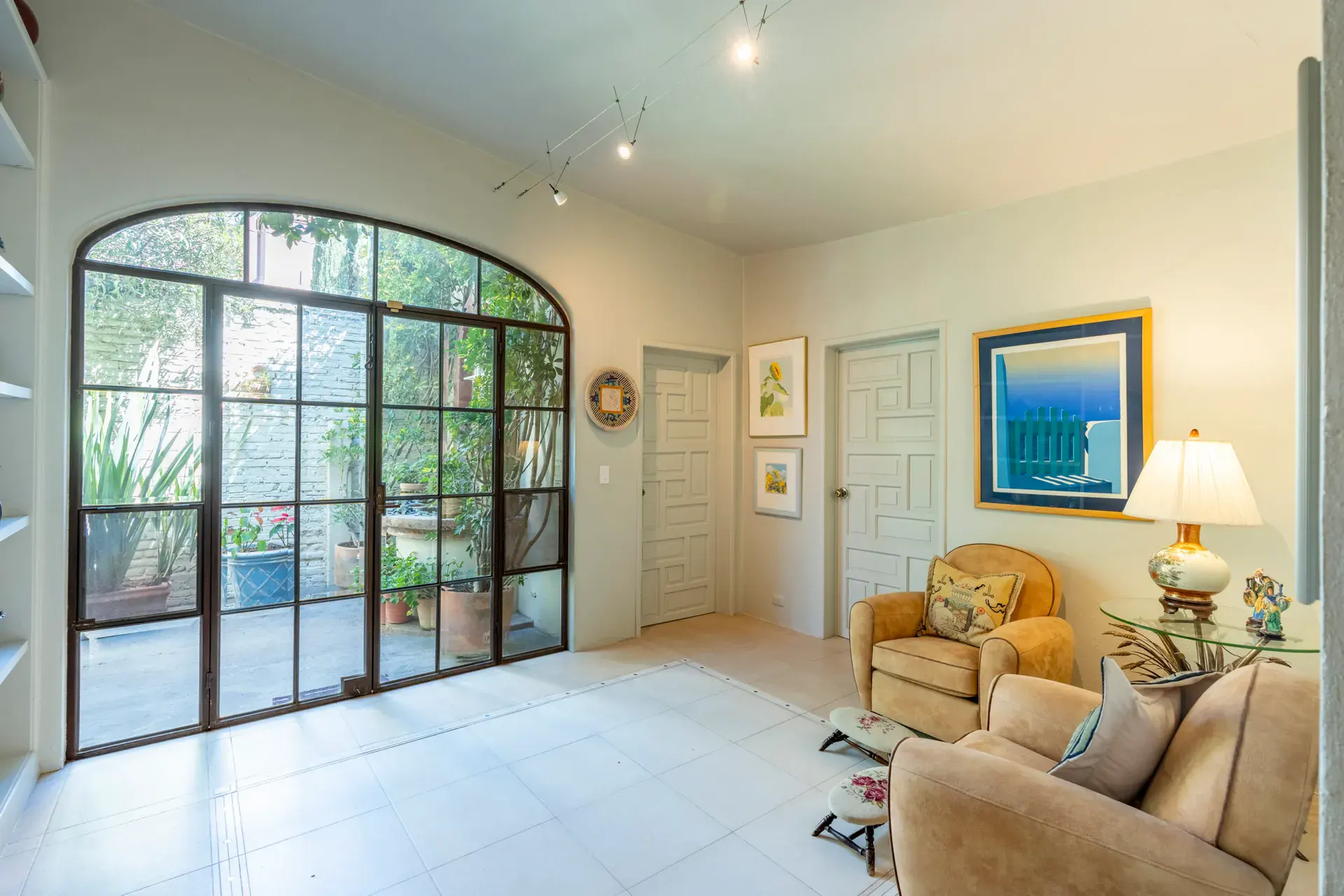 Casa Nispero, foyer with a tall arched steel-framed glass wall to a courtyard and armchairs, San Miguel de Allende