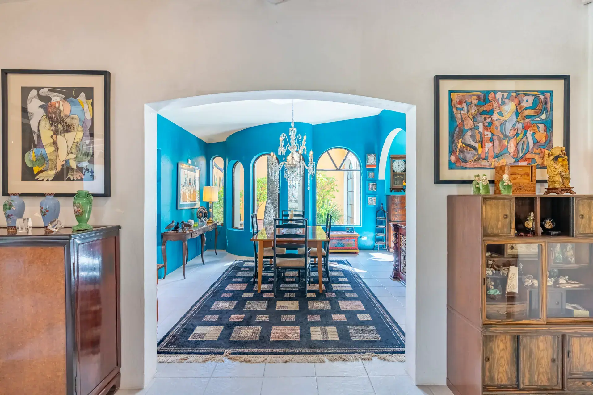 Casa Nispero, view through an arch to a turquoise dining room with a long wood table and a colorful painting, San Miguel de Allende