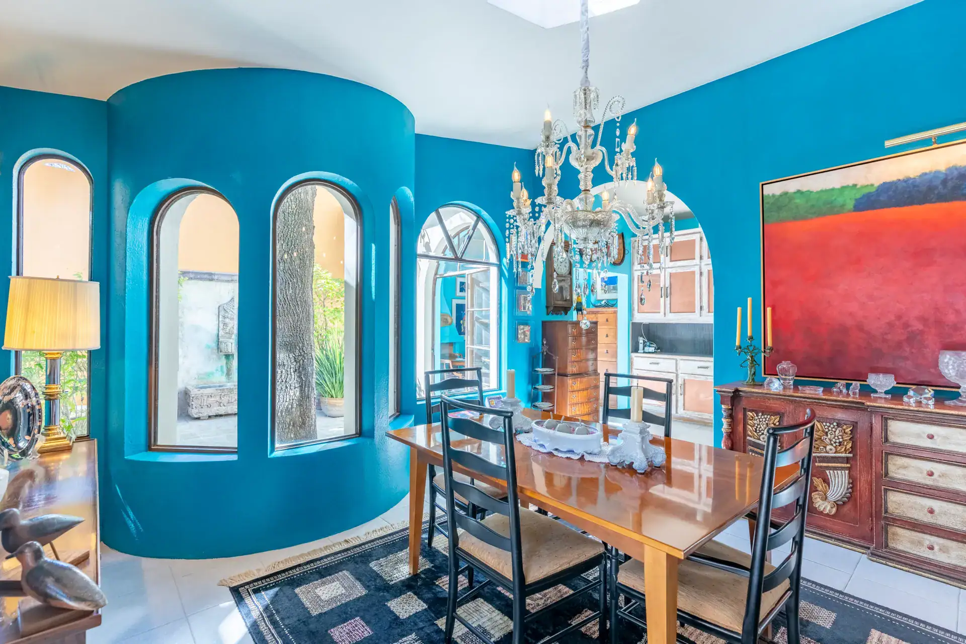 Casa Nispero, turquoise round dining room with arched windows, a crystal chandelier and a large red painting, San Miguel de Allende