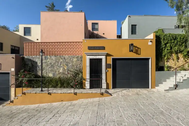 Casa Nobel, street facade with an ochre wall, a black garage door, a stone-clad wall and stone steps, San Miguel de Allende