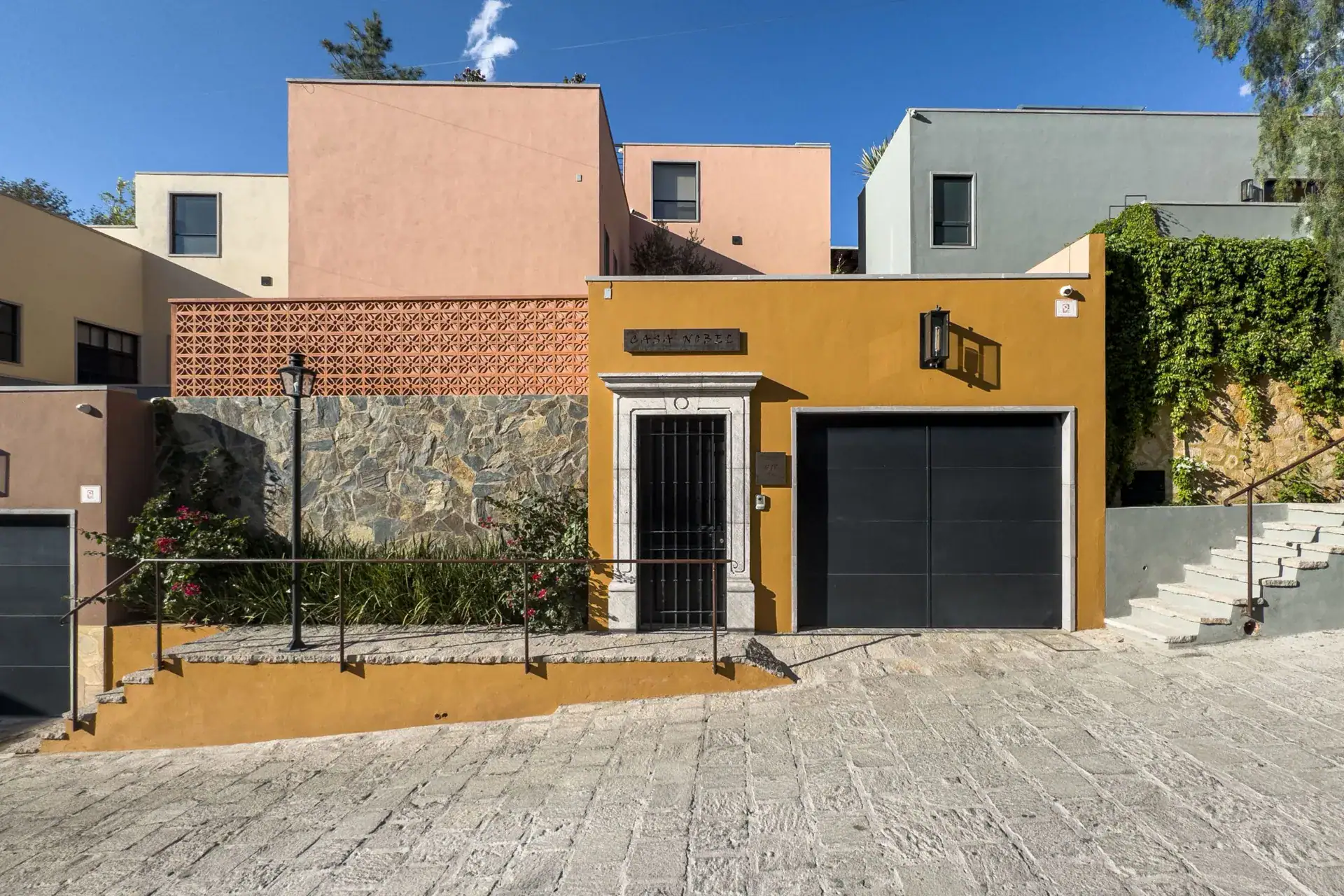 Casa Nobel, street facade with an ochre wall, a black garage door, a stone-clad wall and stone steps, San Miguel de Allende