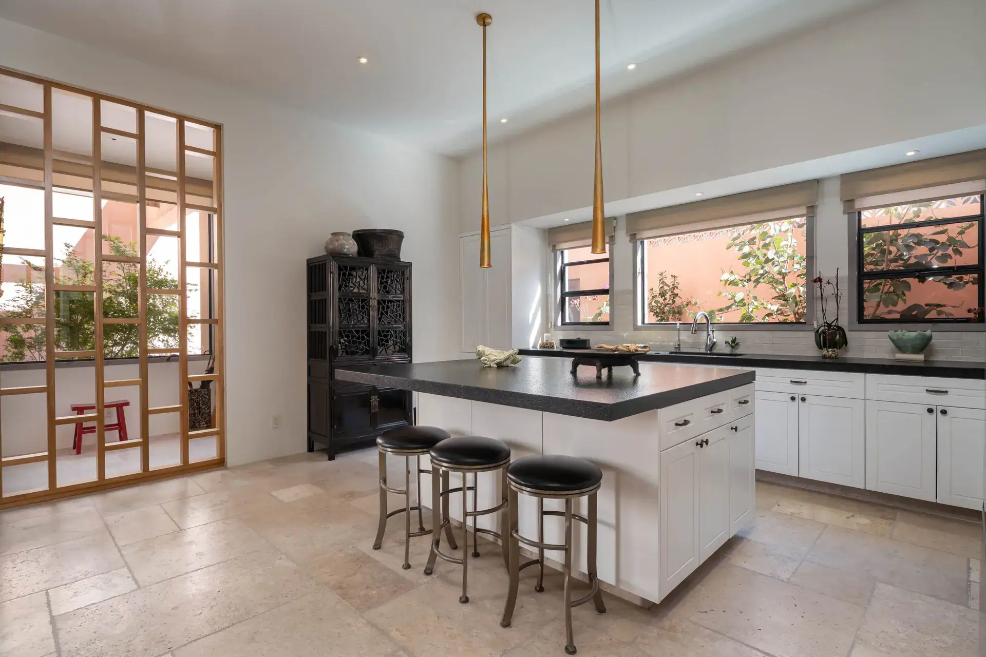 Casa Nobel, kitchen with a white island and black counter, bar stools and a wood lattice screen, San Miguel de Allende