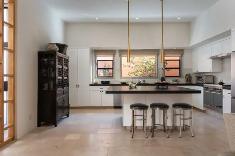 Casa Nobel, kitchen with a long island, pendant lights and windows onto a pink courtyard wall, San Miguel de Allende