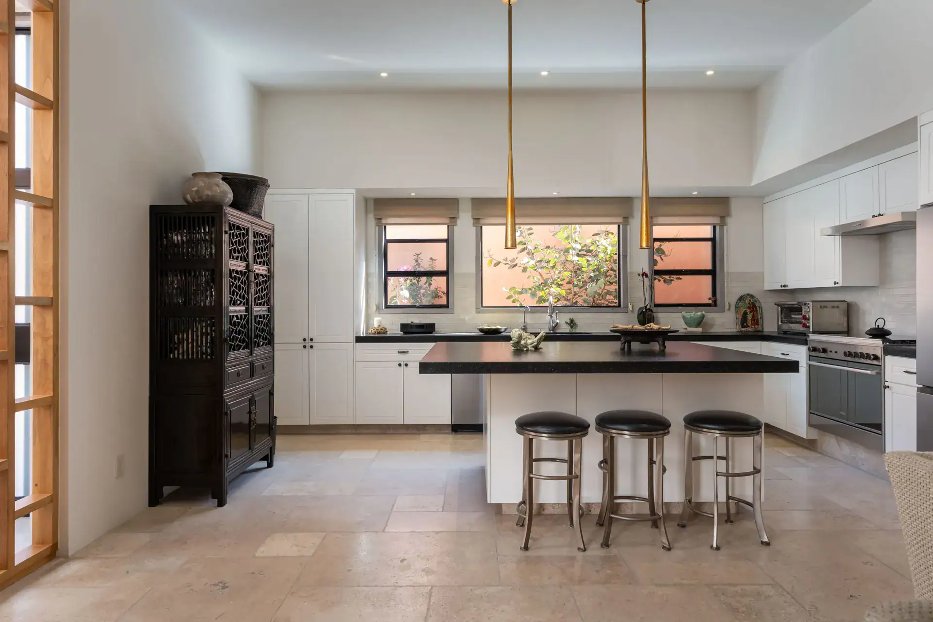 Casa Nobel, kitchen with a long island, pendant lights and windows onto a pink courtyard wall, San Miguel de Allende