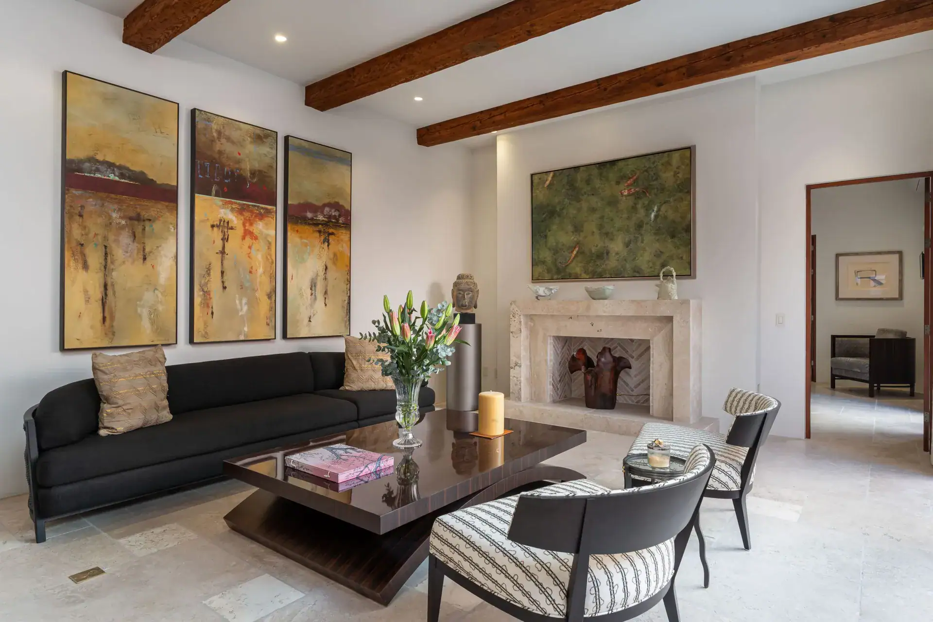 Casa Nobel, living room with a black sofa, a stone fireplace, three golden paintings and a striped chair, San Miguel de Allende