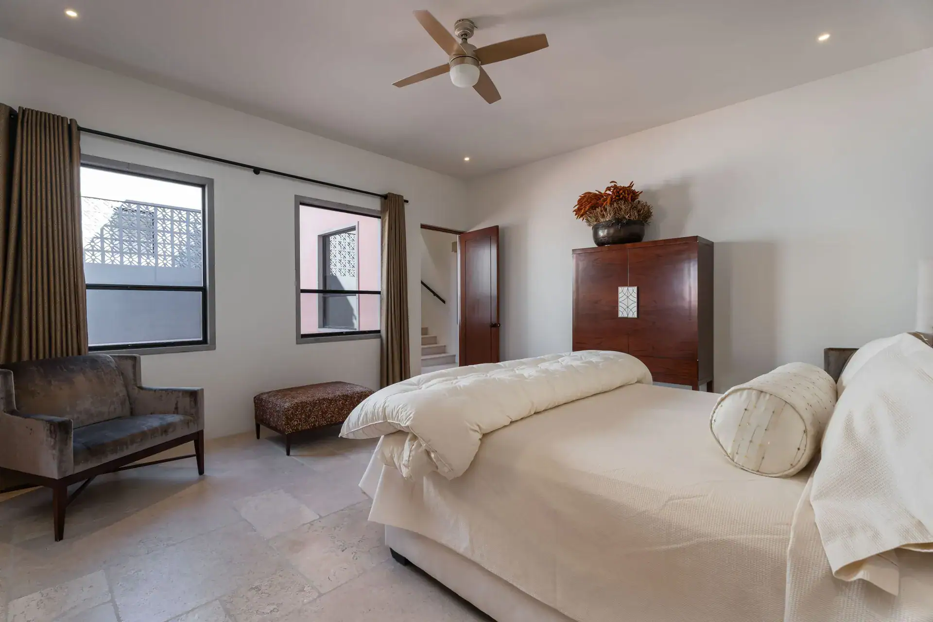 Casa Nobel, bedroom with a cream bed, gray settee and a carved wood armoire, San Miguel de Allende