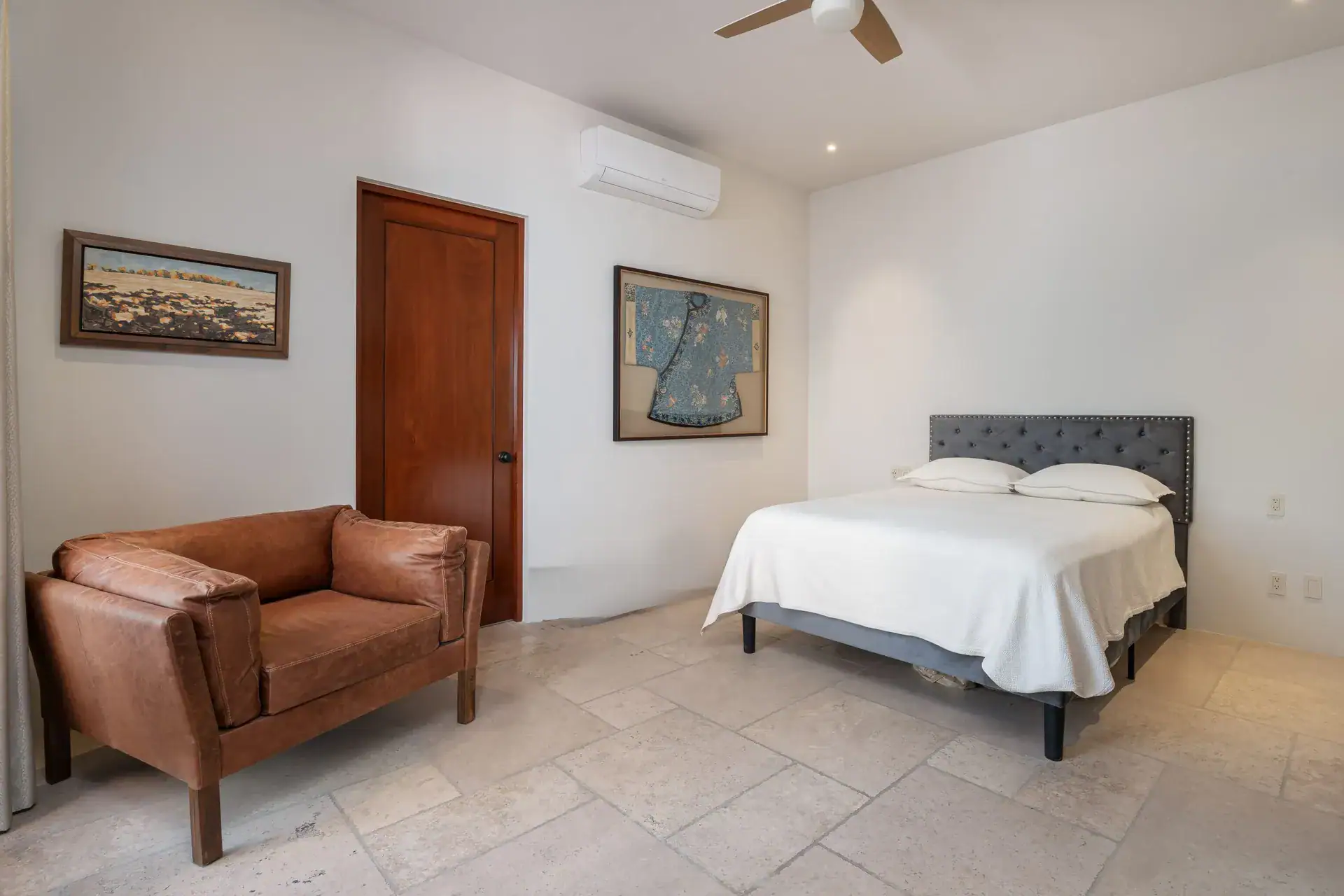 Casa Nobel, bedroom with a brown leather armchair, a gray tufted headboard and a framed robe, San Miguel de Allende