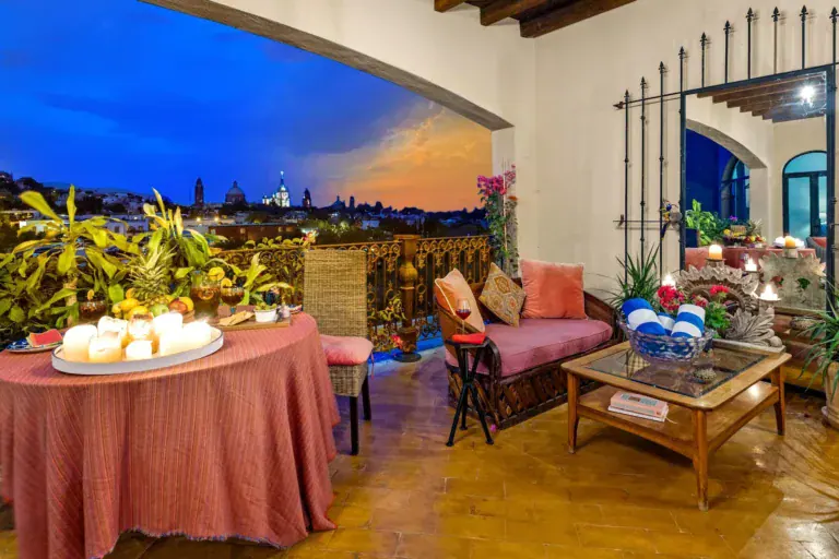 Casa Noche Magica, terrace dining table with a coral cloth and candles at dusk, a daybed and a view of the town's domes, San Miguel de Allende