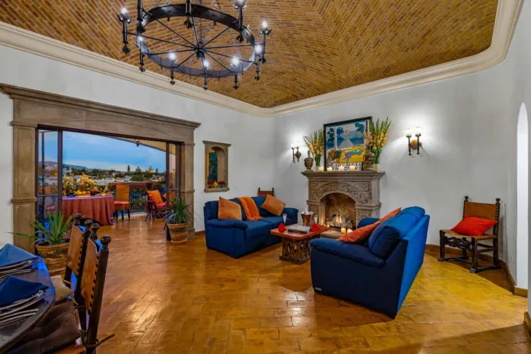 Casa Noche Magica, living room with a brick vaulted ceiling, a stone fireplace, blue sofas and an iron chandelier, opening to a view terrace, San Miguel de Allende