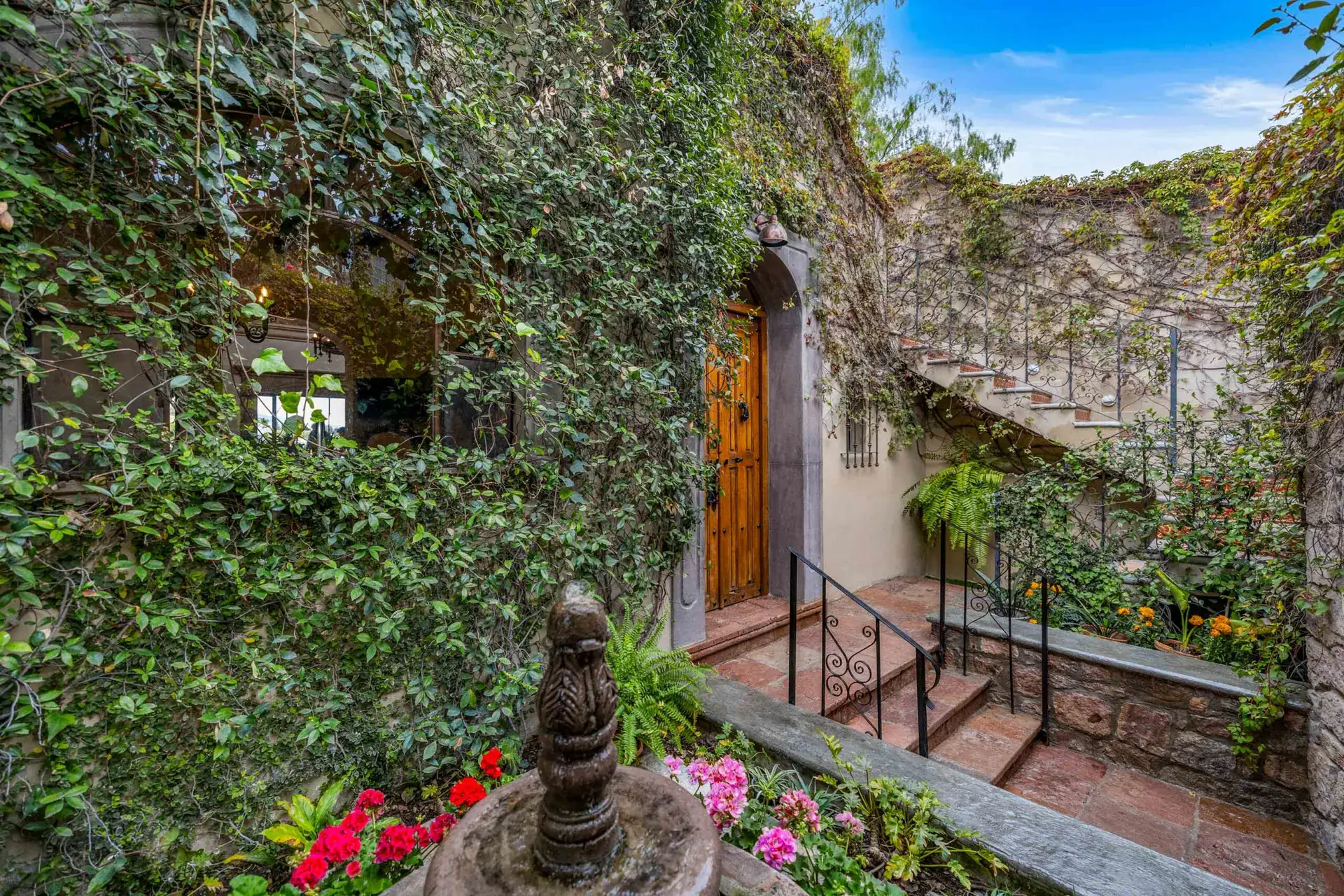 Casa Noche Magica, garden stairway with ivy walls, a wood door, a stone fountain and bright flowers, San Miguel de Allende