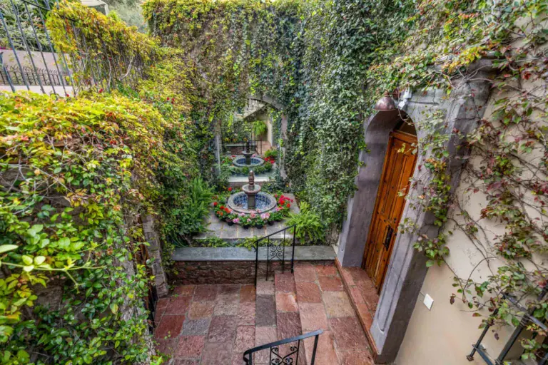 Casa Noche Magica, courtyard fountain surrounded by ivy walls, red flowers and a stairway to an entry door, San Miguel de Allende