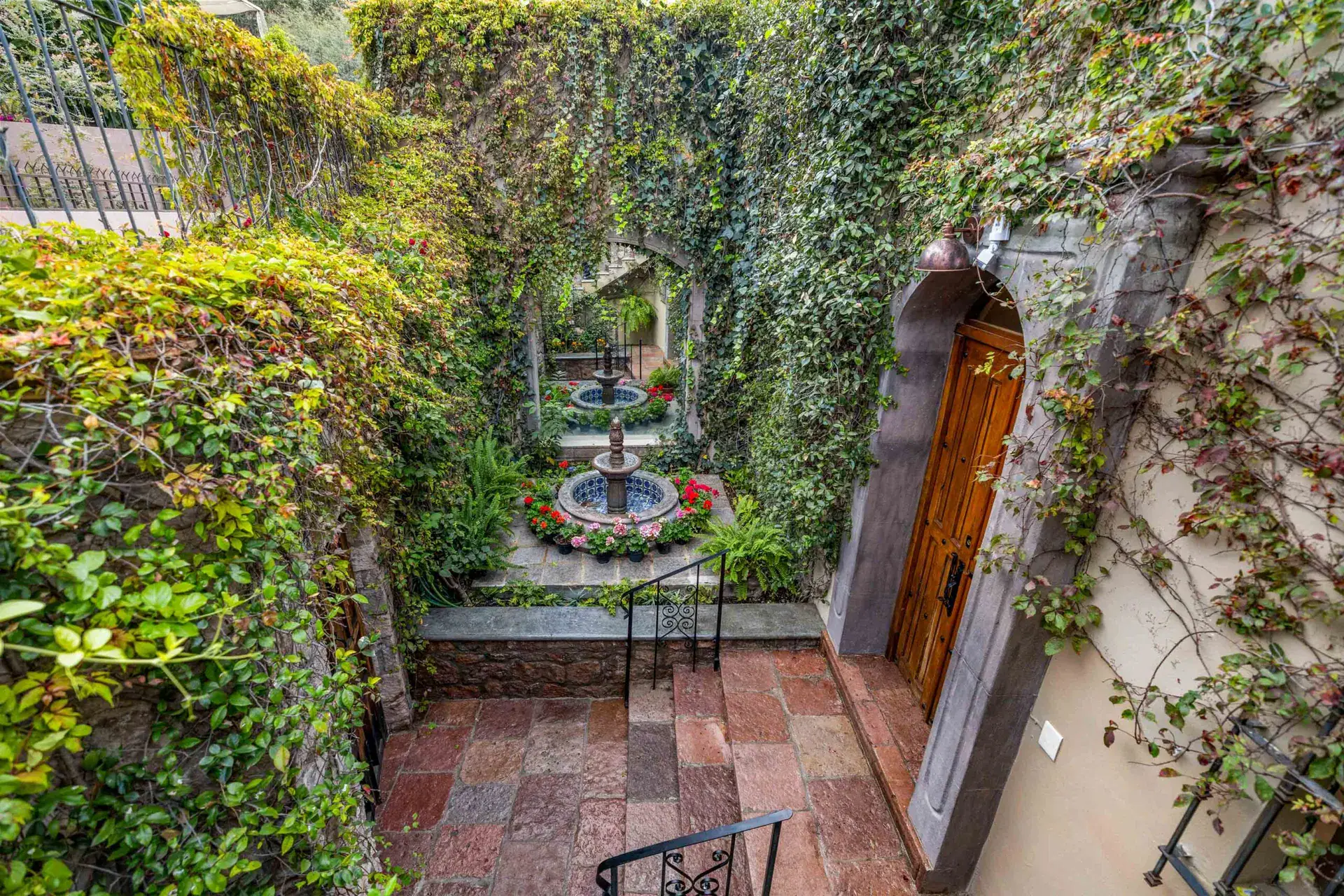 Casa Noche Magica, courtyard fountain surrounded by ivy walls, red flowers and a stairway to an entry door, San Miguel de Allende