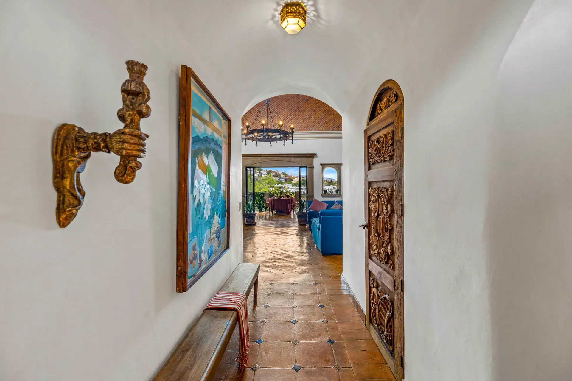 Casa Noche Magica, entry hallway with a carved wood door, a framed painting and a view to the living room, San Miguel de Allende