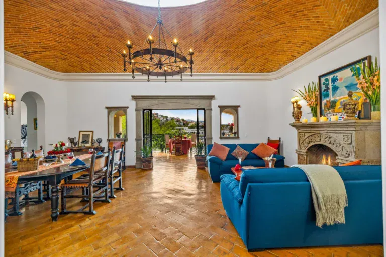 Casa Noche Magica, living room and dining room under a brick vaulted ceiling with a stone fireplace and a long dining table, San Miguel de Allende