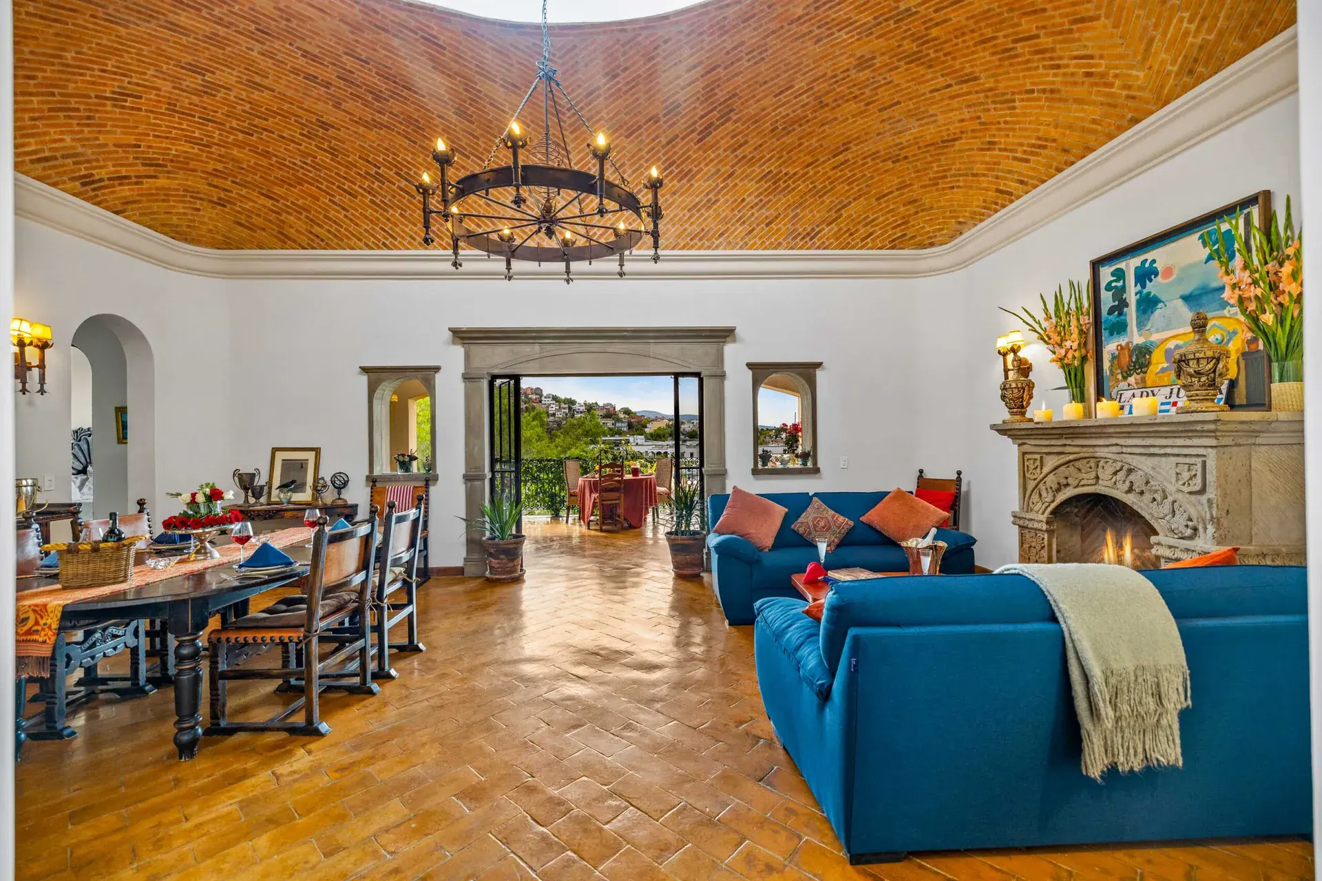 Casa Noche Magica, living room and dining room under a brick vaulted ceiling with a stone fireplace and a long dining table, San Miguel de Allende
