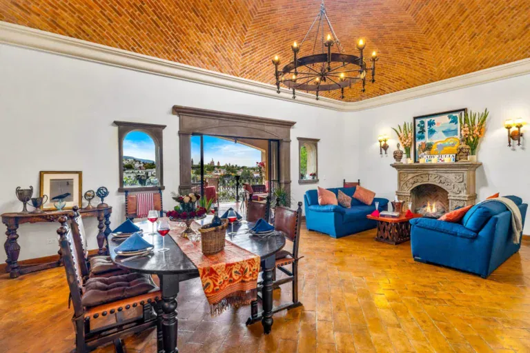 Casa Noche Magica, dining table set for dinner in front of the fireplace and a window with a hillside view, San Miguel de Allende