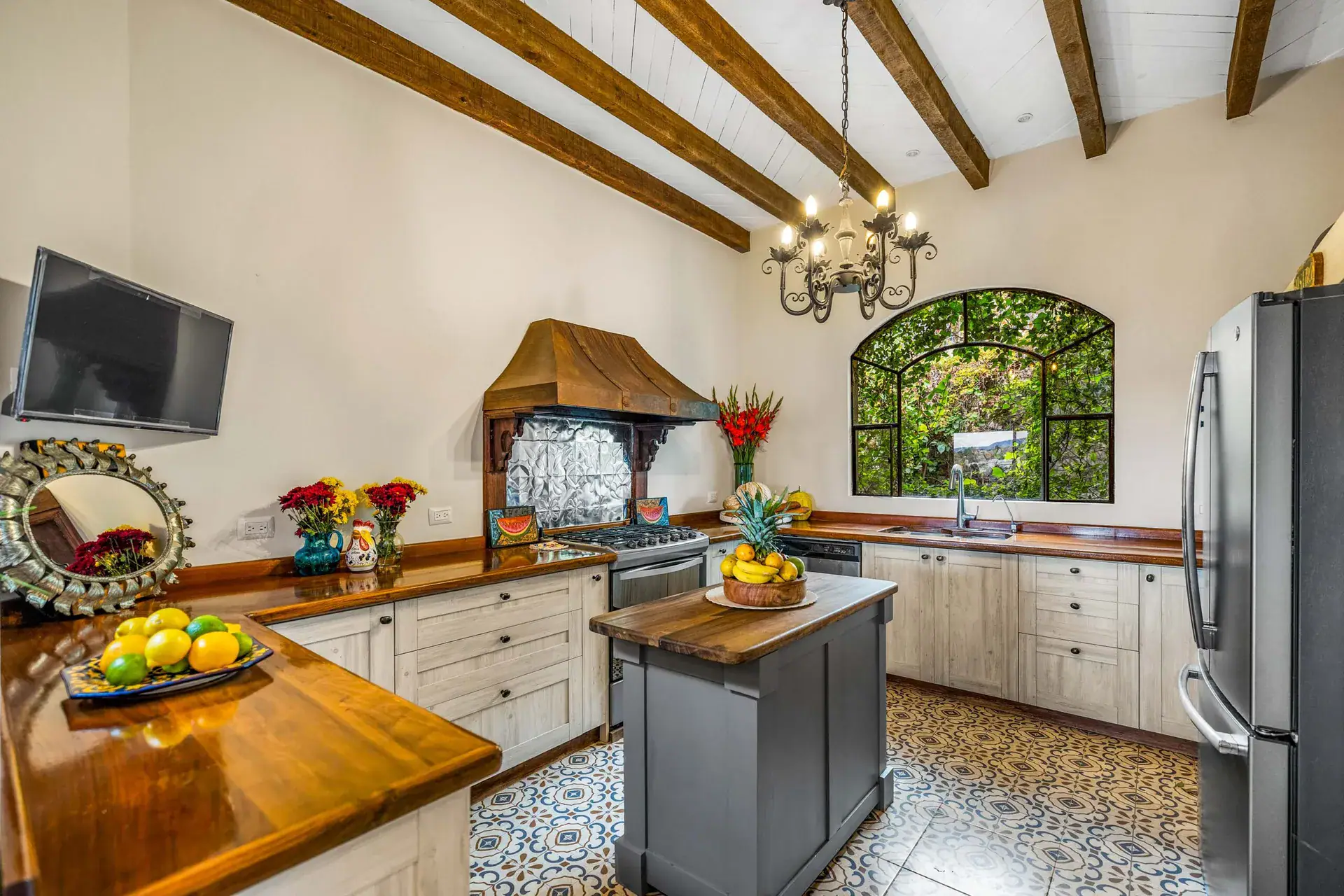Casa Noche Magica, kitchen with a wood island, white cabinets, a copper hood, tile floor and a large window, San Miguel de Allende