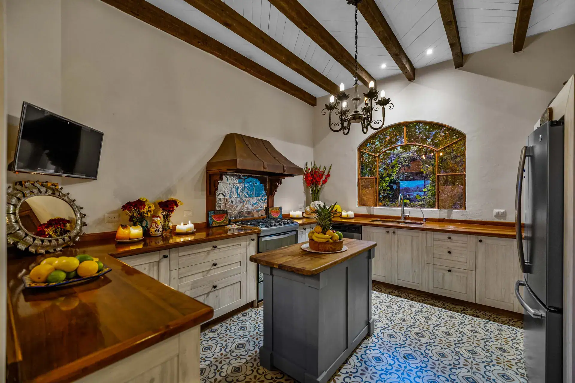 Casa Noche Magica, kitchen with a copper range hood, a stained-glass-style window and a wood-topped island, San Miguel de Allende