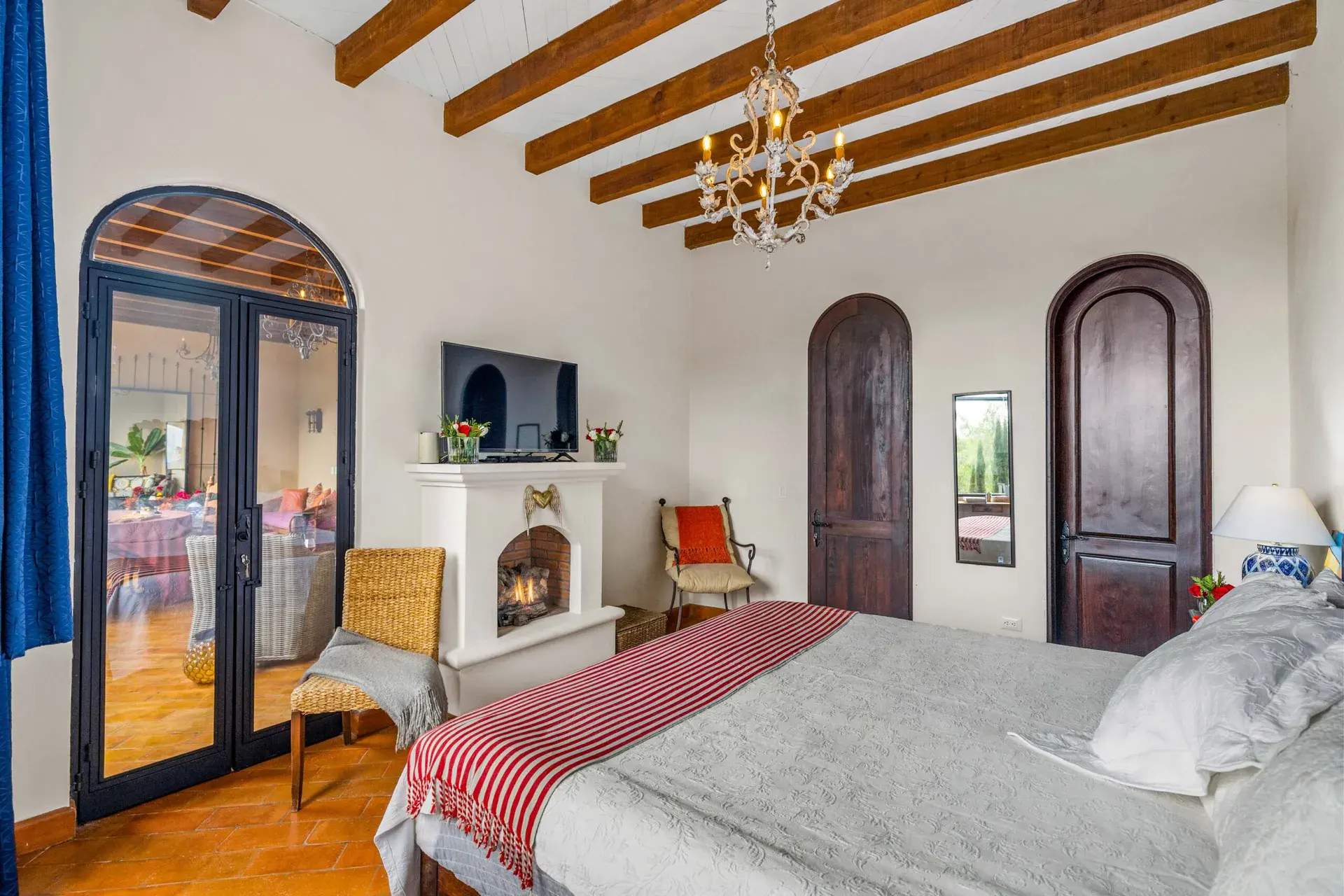 Casa Noche Magica, bedroom with a gas fireplace, a television, glass doors to the terrace and a white and red striped throw, San Miguel de Allende