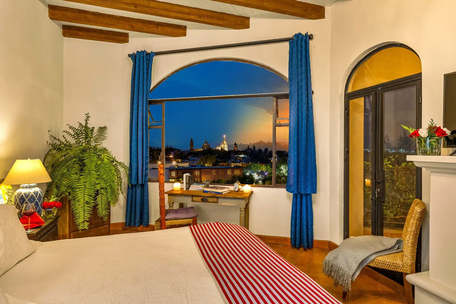 Casa Noche Magica, bedroom at dusk with an arched window facing the glowing sky over the town, San Miguel de Allende