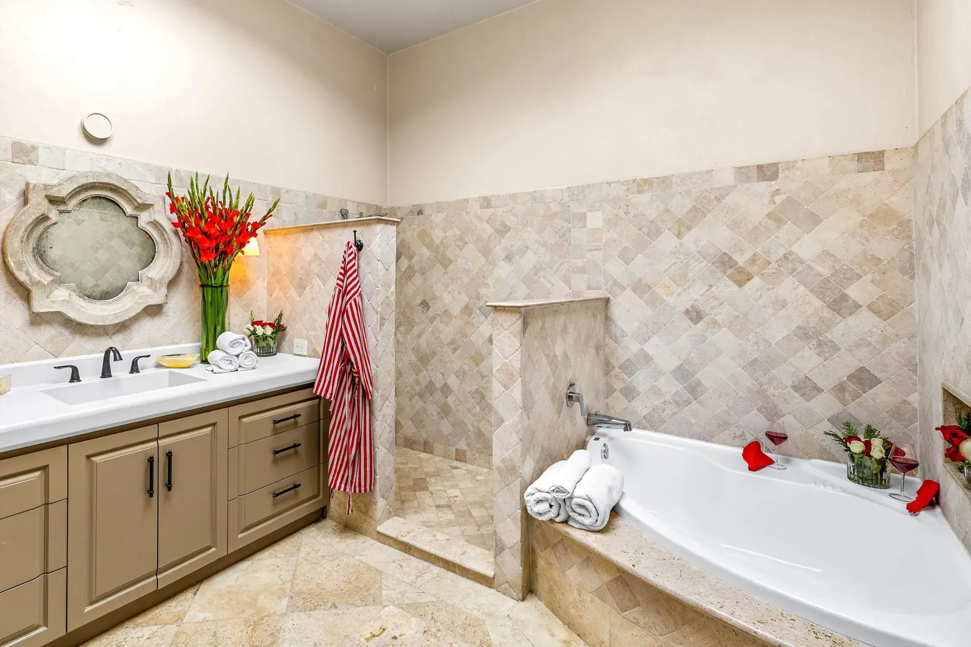 Casa Noche Magica, bathroom with a double vanity, a corner tub, travertine tile and a quatrefoil mirror, San Miguel de Allende