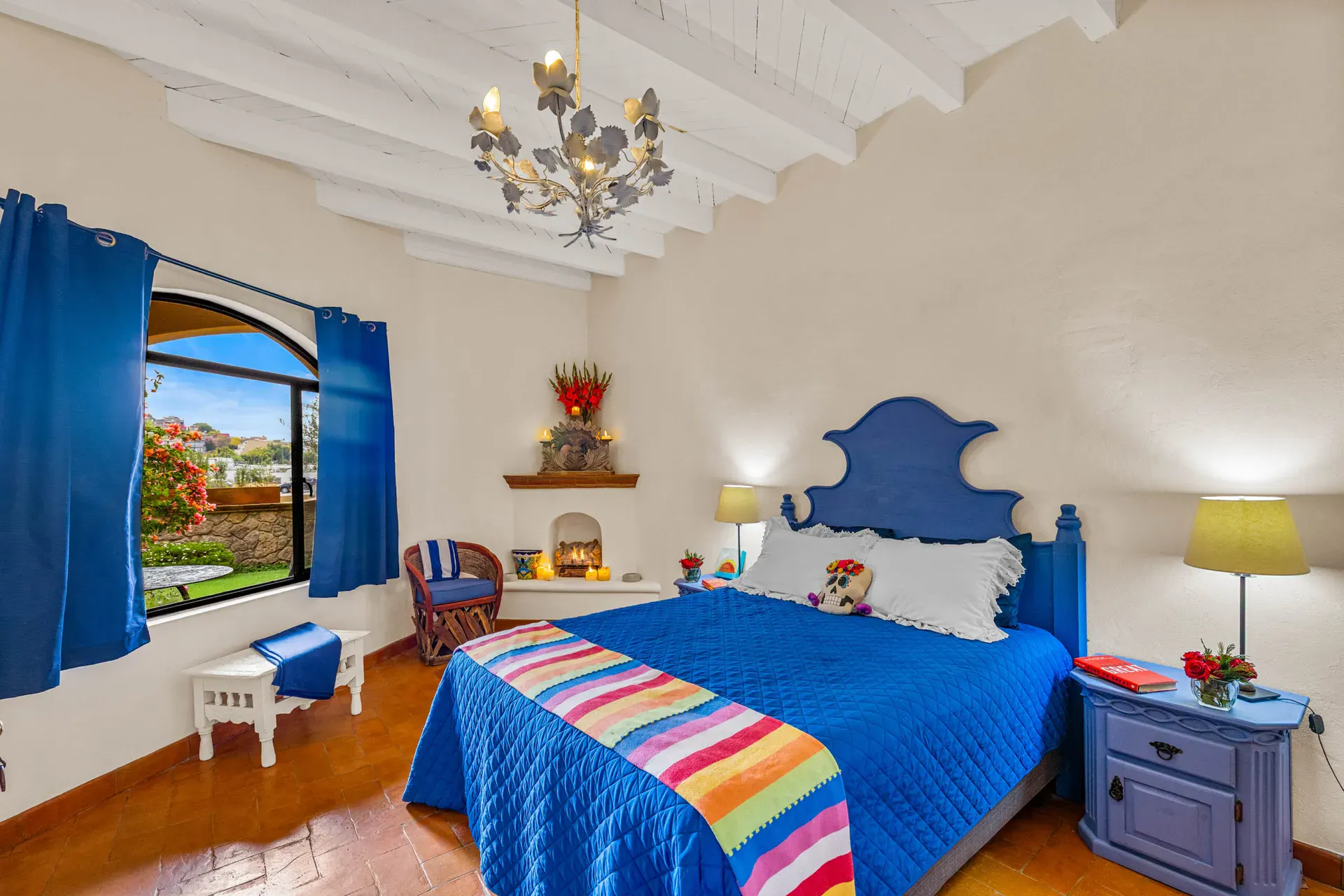 Casa Noche Magica, guest bedroom with a blue headboard, blue bedspread with a rainbow throw and a corner fireplace, San Miguel de Allende