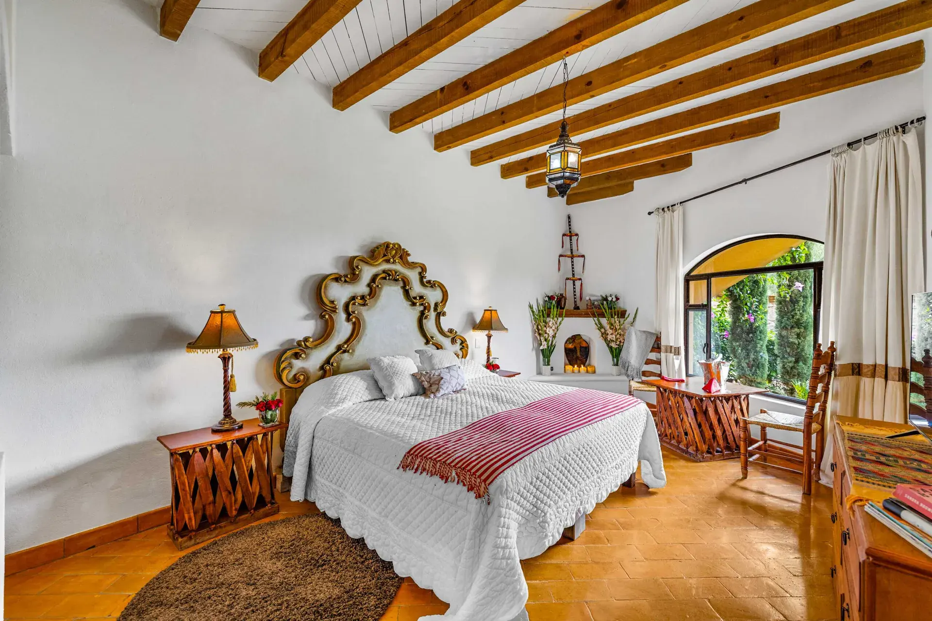 Casa Noche Magica, guest bedroom with an ornate gold headboard, a beamed ceiling and an arched window to the garden, San Miguel de Allende