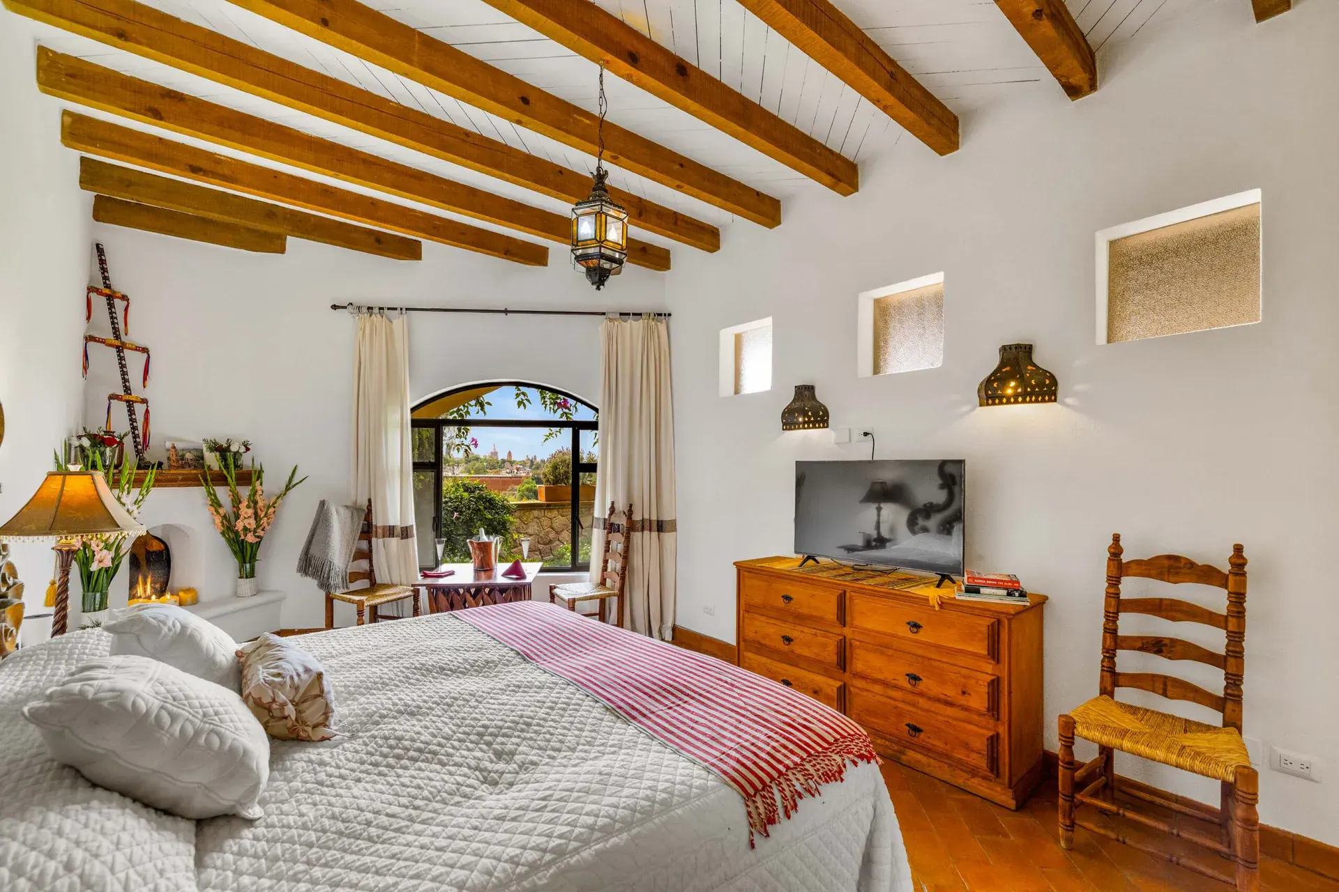 Casa Noche Magica, guest bedroom with a wood dresser, television and an arched window with a garden view, San Miguel de Allende