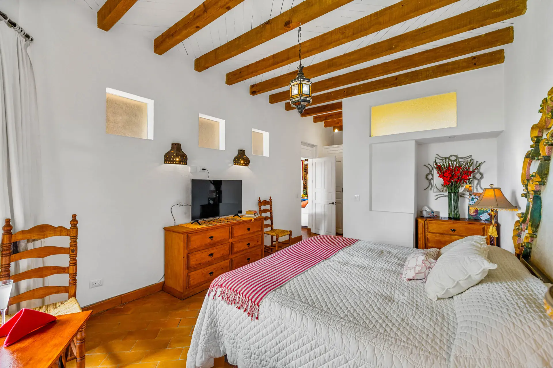 Casa Noche Magica, guest bedroom with a wood dresser, television and ladder-back chairs under a beamed ceiling, San Miguel de Allende