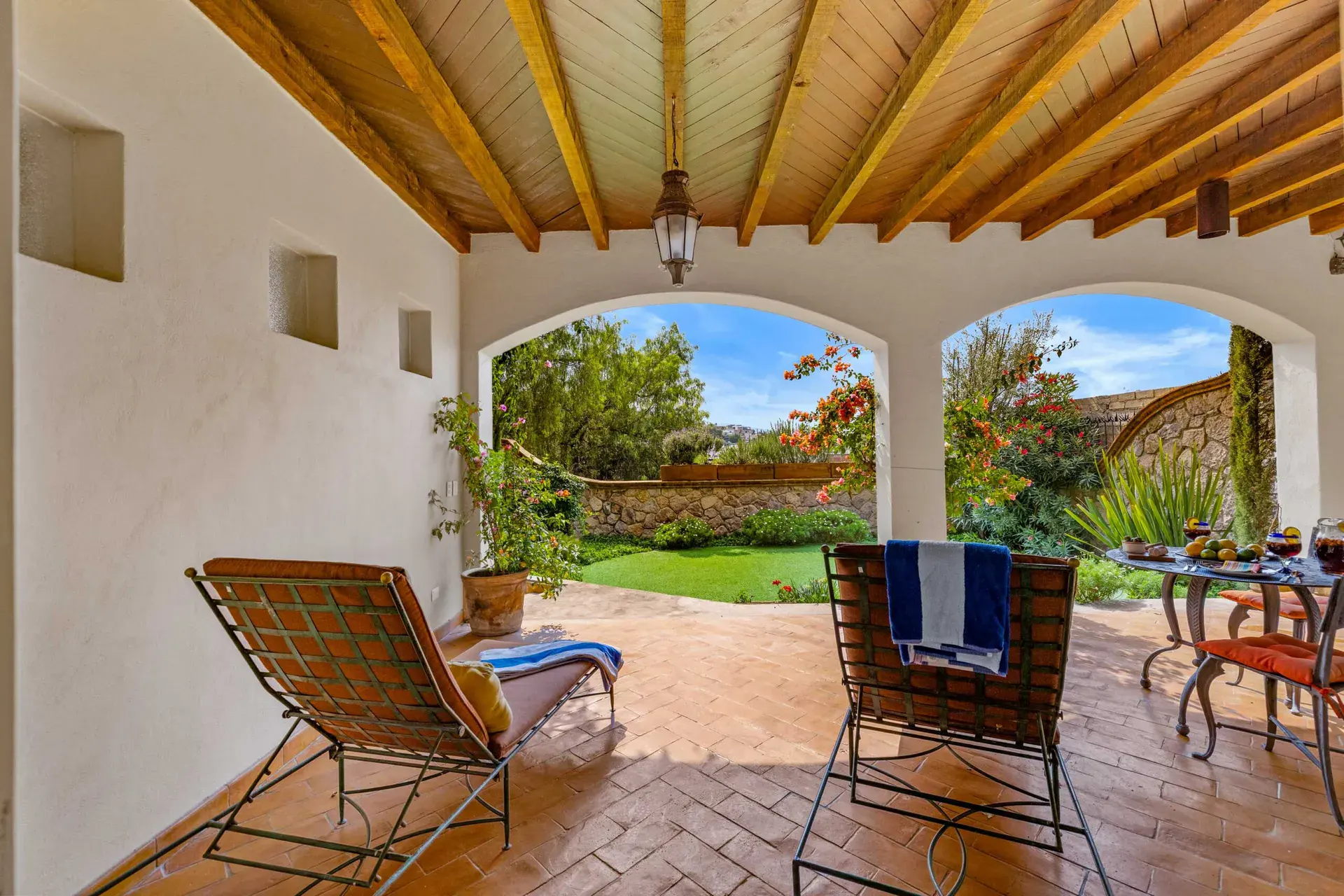 Casa Noche Magica, covered garden terrace with two lounge chairs and a view of the lawn through arches, San Miguel de Allende