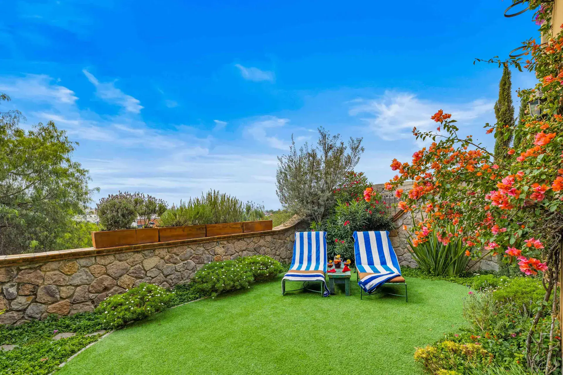 Casa Noche Magica, private lawn with two blue and white striped chairs, a stone wall and flowering shrubs, San Miguel de Allende