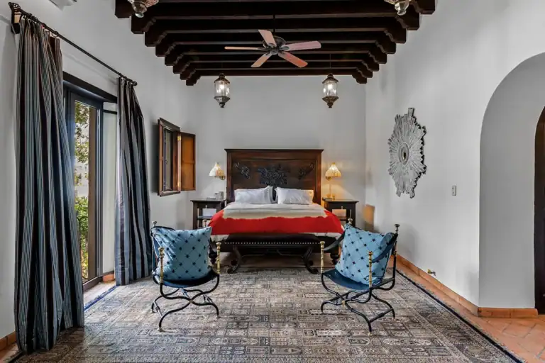 Casa Nola, bedroom with a red bedspread, a wrought-iron balcony and blue chairs, San Miguel de Allende