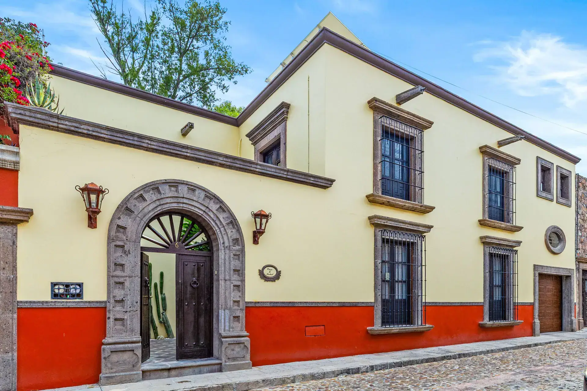 Casa Nostra Familia, yellow and red stucco facade with a stone arched doorway on a cobblestone street, San Miguel de Allende