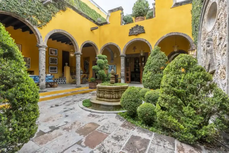 Casa Obelisco, yellow arcaded courtyard with a stone fountain and clipped topiary, San Miguel de Allende