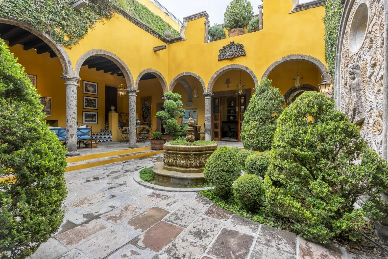 Casa Obelisco, yellow arcaded courtyard with a stone fountain and clipped topiary, San Miguel de Allende