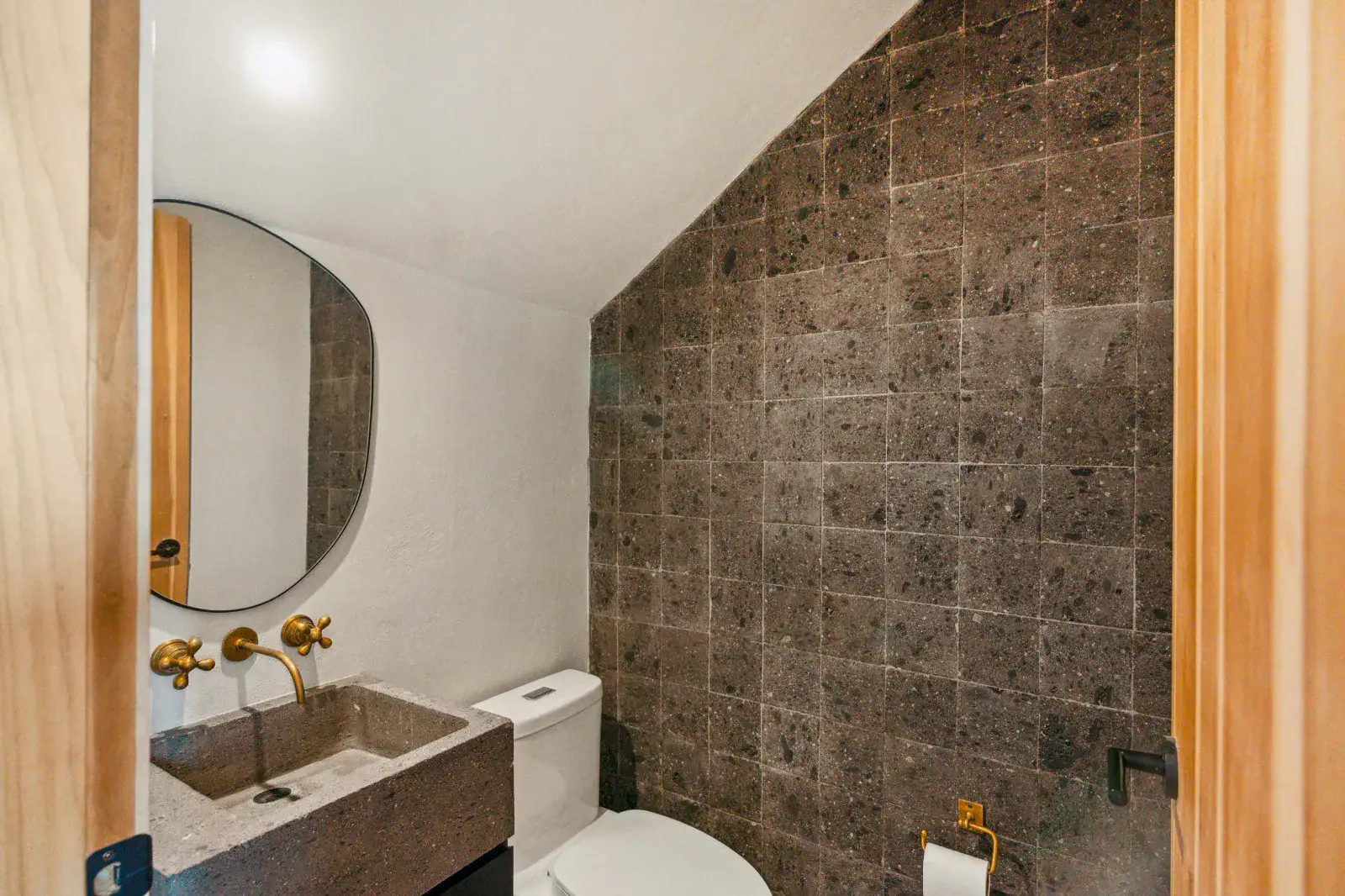 Casa Palma, powder room with a stone wall, a rounded mirror, a stone sink and brass wall faucet, San Miguel de Allende