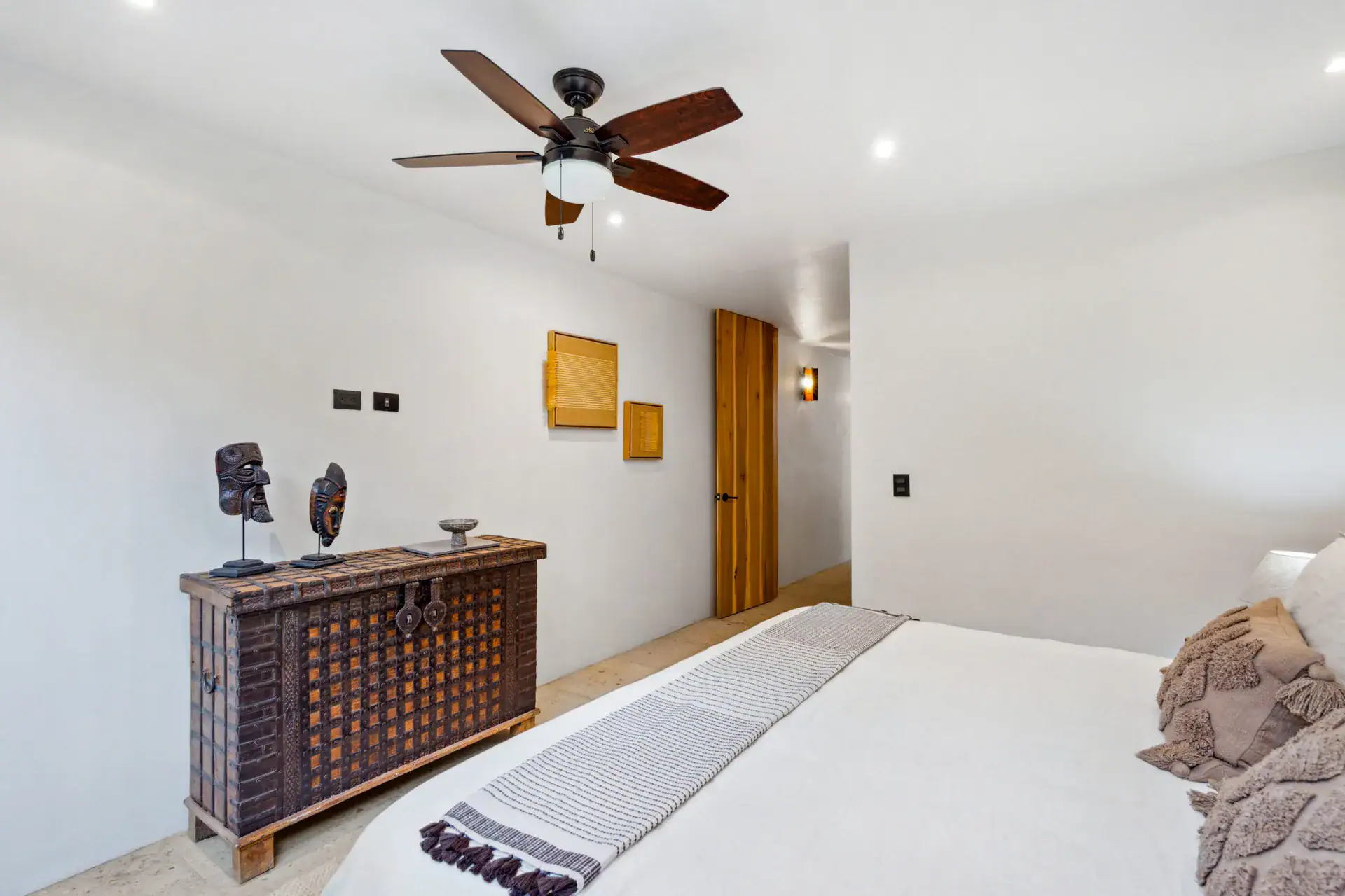 Casa Palma, bedroom with an antique chest with masks, a white bed and a ceiling fan, San Miguel de Allende