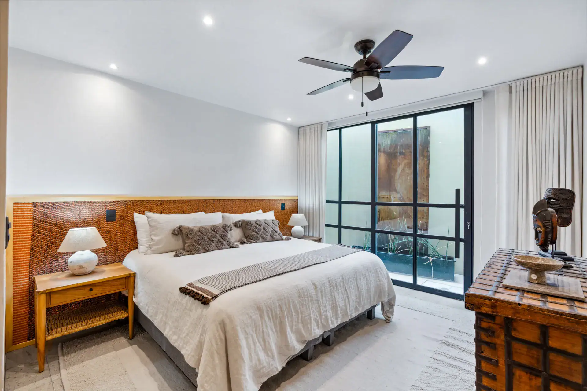 Casa Palma, bedroom with a woven headboard, white bedding and a glass wall to a light well, San Miguel de Allende