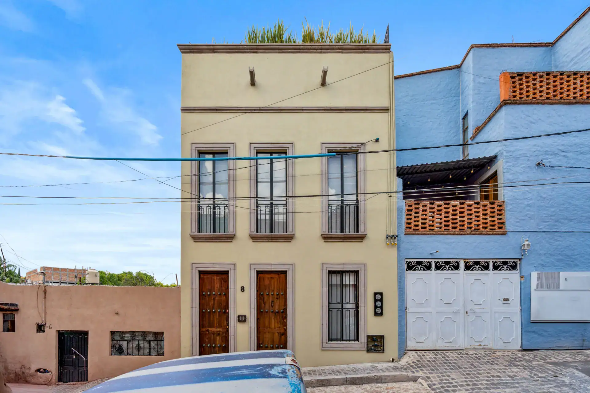 Casa Palma, yellow street facade of the narrow two-story house with wood doors and balconies next to a blue house, San Miguel de Allende
