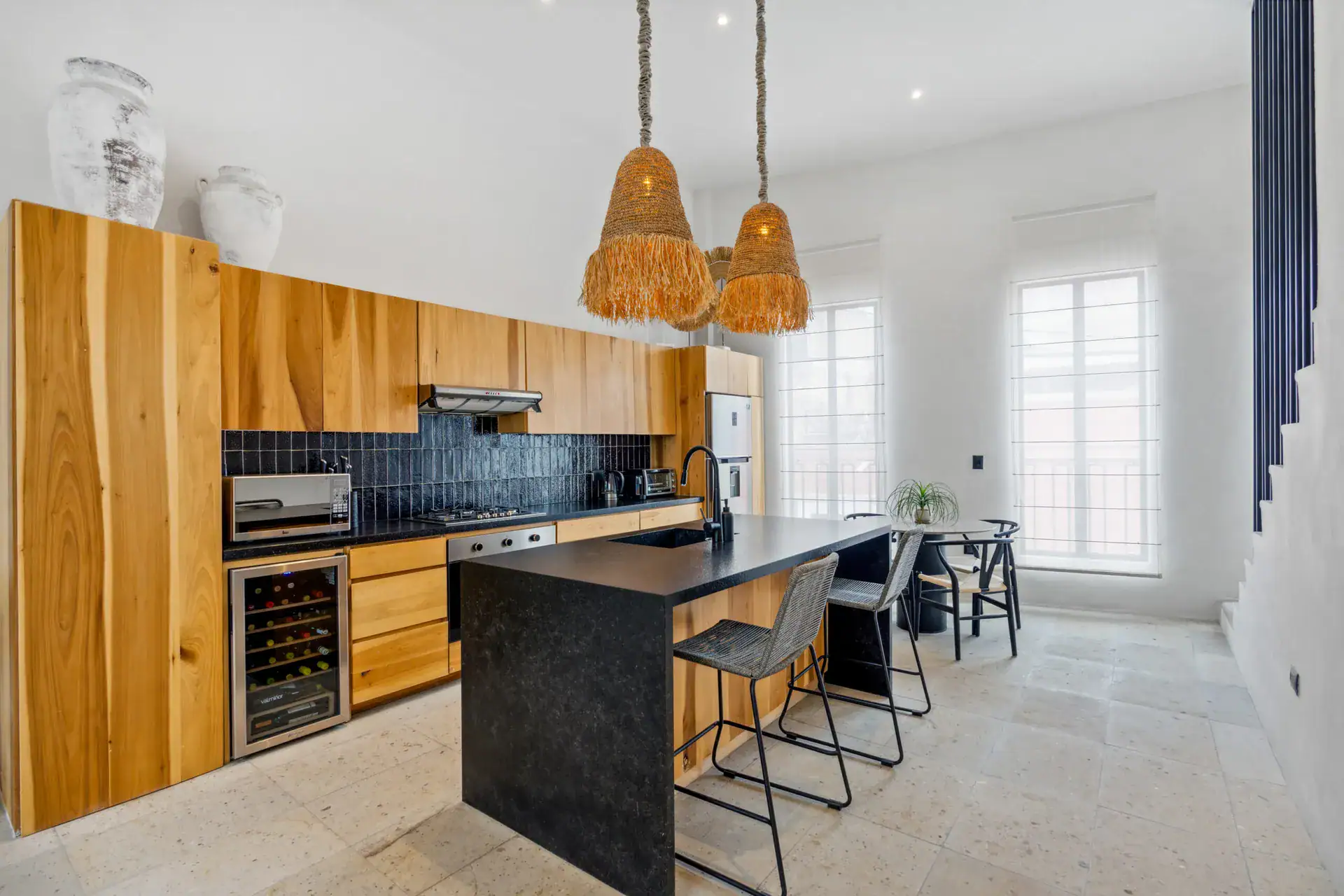 Casa Palma, kitchen with natural wood cabinets, a black bar counter with stools and woven pendant lights, San Miguel de Allende