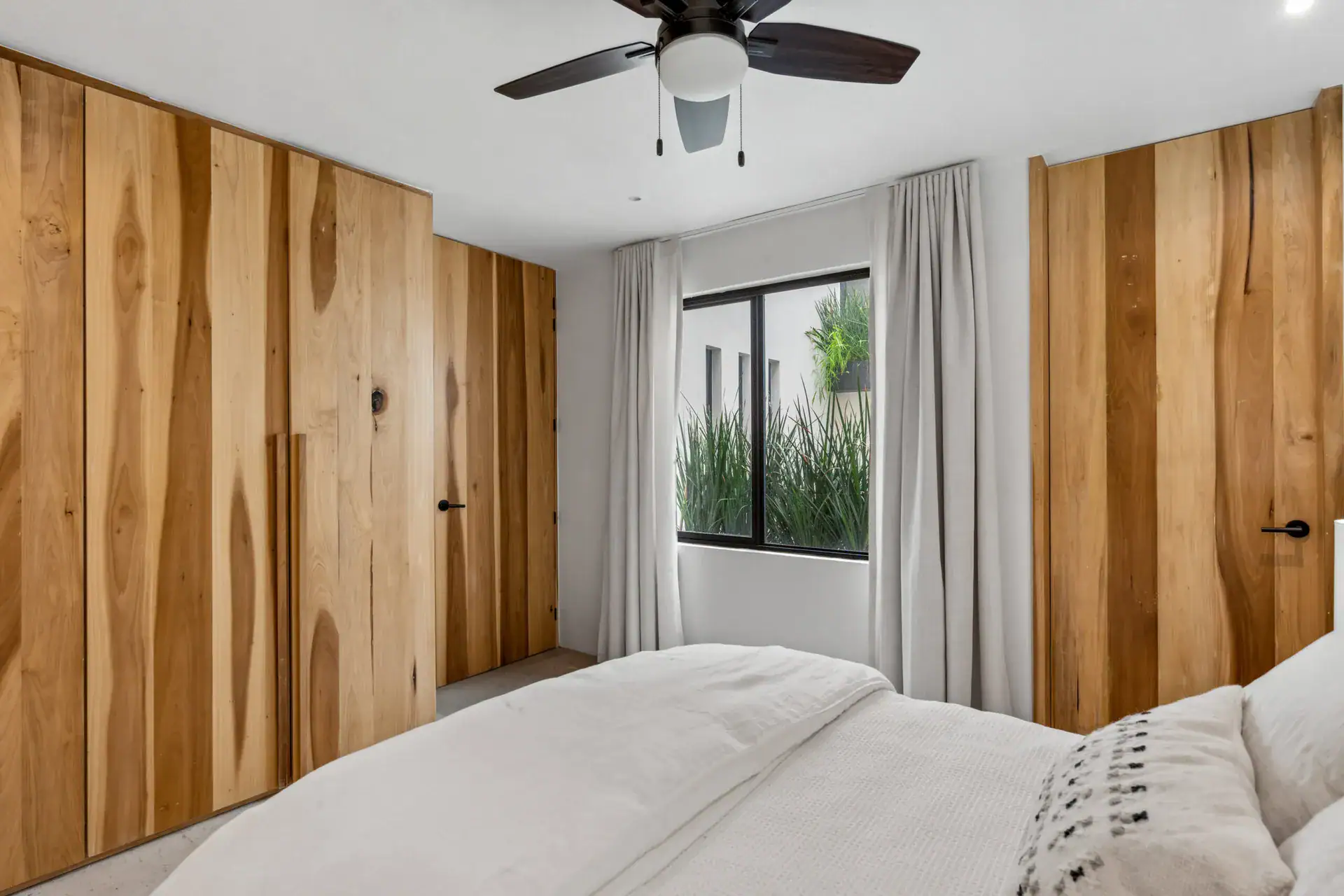 Casa Palma, bedroom with built-in wood wardrobes, a white bed and a window with plants, San Miguel de Allende