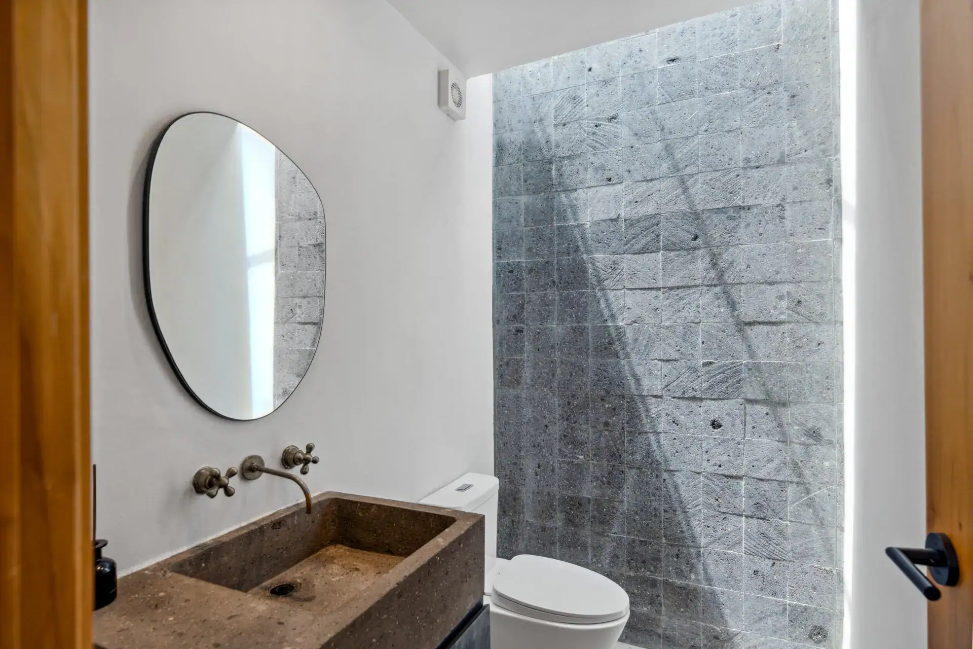 Casa Palma, powder room with a rough stone sink, brass faucet and a rounded mirror beside a stone wall, San Miguel de Allende