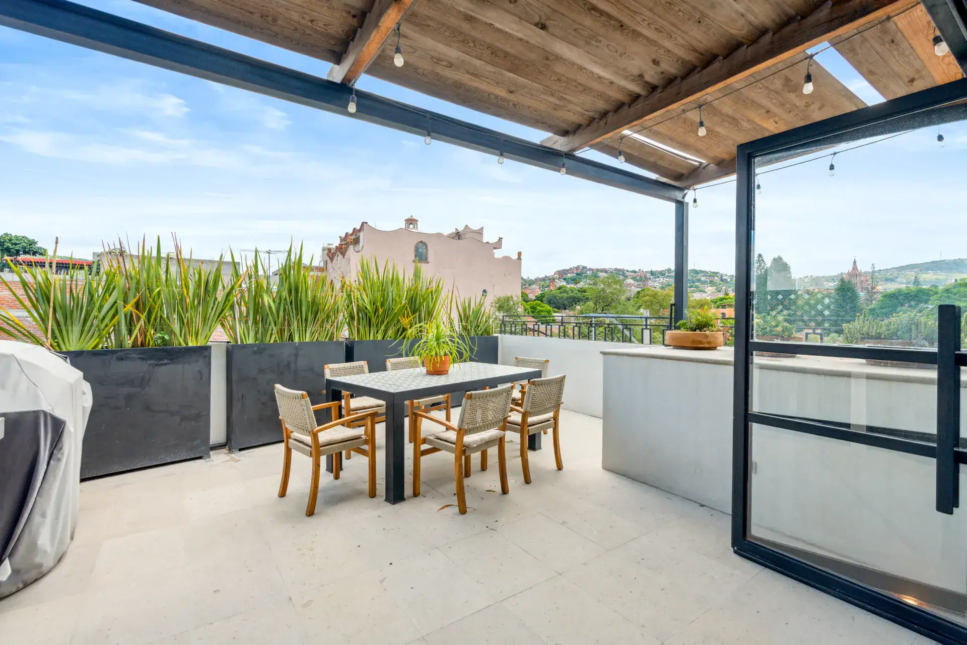 Casa Palma, rooftop terrace with a dining table, steel-framed glass doors, planters and views of the town, San Miguel de Allende