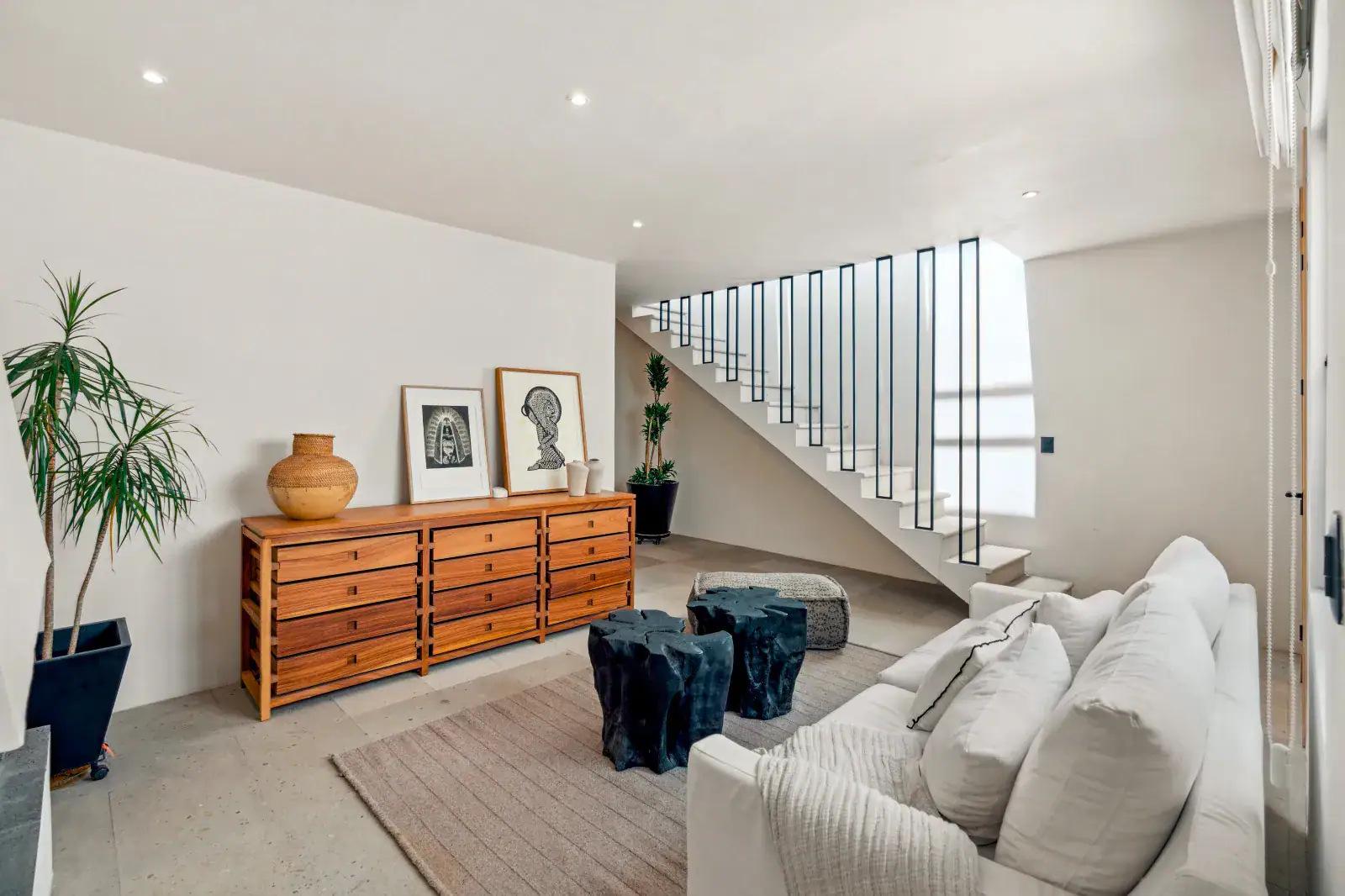 Casa Palma, living room with a white sofa, a wood chest of drawers, black stump tables and a staircase, San Miguel de Allende