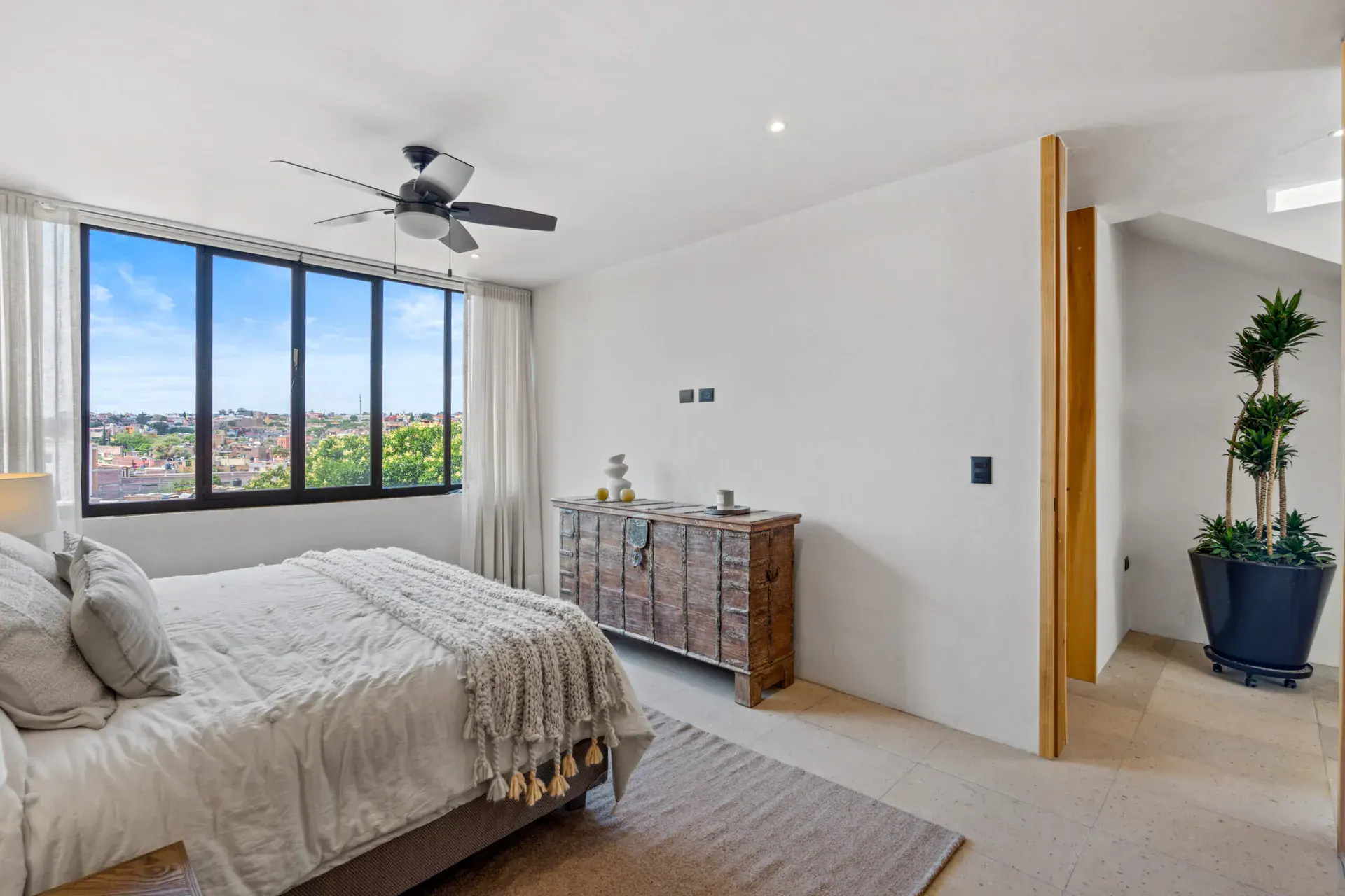 Casa Palma, bedroom with a view of the town through a large window and a wood-framed antique chest, San Miguel de Allende